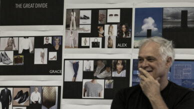 A man with grey hair stands in front of a wall covered with mood boards labelled The Great Divide, Rachael, Alex, and Grace, featuring fashion and lifestyle images. He is smiling with his hand near his mouth.